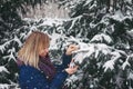 Outdoor winter Christmas portrait of Woman in snowy forest. Smiling Caucasian blonde woman decorates fir tree for the holiday Royalty Free Stock Photo
