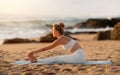 Outdoor workout. Young caucasian woman training outside, stretching leg muscles, exercising on sports mat on sea beach Royalty Free Stock Photo