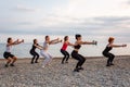 Outdoor yoga and fitness. Side view of group of Caucasian adult fit women are training with dumbbells on pebble beach Royalty Free Stock Photo