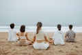 Outdoor yoga and meditation class. Group of young men and women doing breathing exercises on the beach, back view Royalty Free Stock Photo