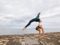 Outdoor yoga practice near the ocean. Young woman practicing Adho Mukha Vrksasana. Yoga Handstand is an inverted asana. Beautiful Royalty Free Stock Photo