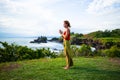 Outdoor yoga practice. Young woman standing on the grass. Hands in namaste mudra, closed eyes. Tanah Lot temple, Bali Royalty Free Stock Photo