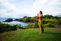 Outdoor yoga practice. Young woman standing on the grass. Hands in namaste mudra, closed eyes. Tanah Lot temple, Bali Royalty Free Stock Photo