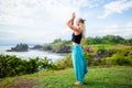 Outdoor yoga practice. Young woman standing on the grass. Hands raising up in namaste mudra, closed eyes. Tanah Lot temple, Bali Royalty Free Stock Photo