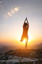 Outdoor yoga silhouette, young woman in tree pose. A woman practices yoga on the green grass on top of a mountain with a Royalty Free Stock Photo