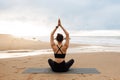 Outdoor yoga. Woman meditating with hands clasped above head, practicing meditation near ocean, back view Royalty Free Stock Photo