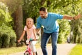 Outdoors activities. Happy father teaching his daughter to ride a bike in the park, enjoying time together on weekend Royalty Free Stock Photo