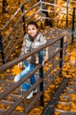 Outdoors fashion portrait of cute young woman walking in autumn park. Model girl with a bright orange autumn leaf in hand climbs Royalty Free Stock Photo