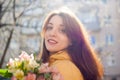Outdoors female portrait of attractive brunette girl in yellow jacket holding a big bouquet of colorful flowers enjoying Royalty Free Stock Photo