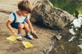 Outdoors image of cute little boy launches paper ship on the lake in the park. Adorable kid boy playing with a boat. Child sailing Royalty Free Stock Photo