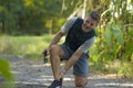 Outdoors jogging accident - young attractive runner man in sport suffering ankle problem during running workout in city park Royalty Free Stock Photo