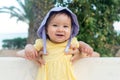 outdoors lifestyle portrait of adorable and happy baby girl in cute hat hold by her mothers hands on park bench looking excited Royalty Free Stock Photo