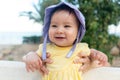outdoors lifestyle portrait of adorable and happy baby girl in cute hat hold by her mothers hands on park bench looking excited Royalty Free Stock Photo