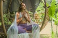 Outdoors natural portrait of young beautiful and happy girl practicing yoga workout sitting on gazebo in lotus meditation pose at