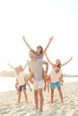 Outdoors photo of joyful smiling boyfriends piggybacking their girlfriends while rise hands at sunset on beach Royalty Free Stock Photo