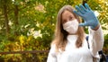 Outdoors portrait of beautiful young woman wearing cotton white mask and medicalgloves greeting and say hello, Nature and trees in