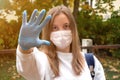 Outdoors portrait of beautiful young woman wearing cotton white mask and medicalgloves greeting and say hello, Nature and trees in