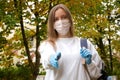 Outdoors portrait of beautiful young woman wearing cotton white mask and medicalgloves greeting and say hello, Nature and trees in