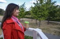 Outdoors portrait of cheerful beautiful brunette woman in red coat holding disposable coffee cup drinking coffee, and smiling Royalty Free Stock Photo