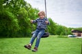 Outdoors portrait of cute preschool laughing boy swinging on a swing at the playground