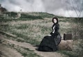 Outdoors portrait of a victorian lady in black sitting alone on the road with her luggage Royalty Free Stock Photo