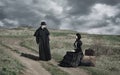 Portrait of a victorian lady in black sitting on the road with her luggage and gentleman standing nearby. Royalty Free Stock Photo