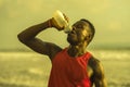 Outdoors portrait of young athletic and fit african american sport man drinking water after hard running workout at the beach Royalty Free Stock Photo