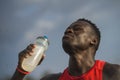 Outdoors portrait of young athletic and fit african american sport man drinking water after hard running workout hydrating and Royalty Free Stock Photo