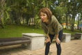 Outdoors portrait of young attractive tired and breathless jogger woman in breathing exhausted after running workout at beautiful