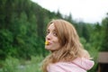 Outdoors portrait of young calm blonde woman in pink clothes with little yellow flower in her mouth on the hill with Royalty Free Stock Photo