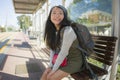 Outdoors portrait of young happy and beautiful Asian Chinese tourist woman with backpack sitting cheerful on train station bench Royalty Free Stock Photo