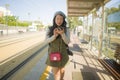 Outdoors portrait of young happy and beautiful Asian Chinese tourist woman with backpack using mobile phone on train station Royalty Free Stock Photo