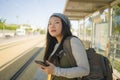 Outdoors portrait of young happy and beautiful Asian Chinese tourist woman with backpack using mobile phone on train station Royalty Free Stock Photo