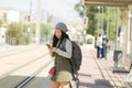 Outdoors portrait of young happy and beautiful Asian Korean tourist woman with backpack using mobile phone on train station Royalty Free Stock Photo