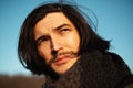 Outdoors portrait of young thoughtful man with long hair on blue sky background. Artistic concept. Royalty Free Stock Photo