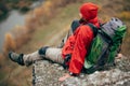 Outdoors rear view of tired hiker man in red clothes sitting on the rock relaxing after hiking in mountain. Royalty Free Stock Photo