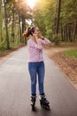 Outdoors shot of woman listening to music open air while spending time in forest, adorable female posing on asphalt road in wood, Royalty Free Stock Photo