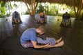 Outdoors yoga lesson - group of young people and coach man practicing relaxation exercise at Asian wellness retreat hut training