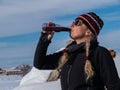 An outdoorsy Caucasian woman in pigtails and winter clothes, drinking soda in a snowy setting