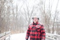 Outdoorsy man in plaid walking over bridge during snowfall