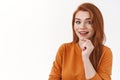 Outgoing good-looking redhead woman in orange sweater, touchin chin thoughtful, pondering something curious, smiling Royalty Free Stock Photo