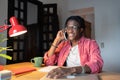 Outgoing smiling African American man talking on mobile phone making call sits at desk in room Royalty Free Stock Photo