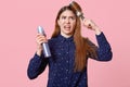 Outraged Caucasian woman has angry expression, combs unmanageable hair, dissatisfied with new conditioner, holds hairspray, fails