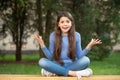 Outraged girl teenager shrugging shoulders sitting legs crossed on bench outdoors, outrage