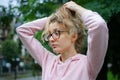 Outside portrait of blonde girl with hipster eyeglasses in pink clothes making ponytail outdoors in the urban park