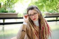 Outside portrait of young independent woman in eyeglasses, casual nude trench with long dreadlocks sitting in outdoor