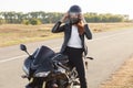 Outside shot of fast female motorcyclist wears protective helmet, poses on motorbike, stands on motorbike, covers long distance,