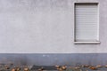 Outside wall, closed window, aged stucco plaster and gray founda