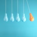 Outstanding orange light bulb hanging among light blue light bulb on blue background.