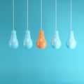 Outstanding orange light bulb hanging among light blue light bulb on blue background.